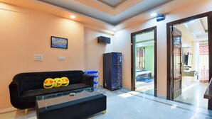 A modern lobby with a black sofa, a glass coffee table, a black refrigerator, and a television on the wall.