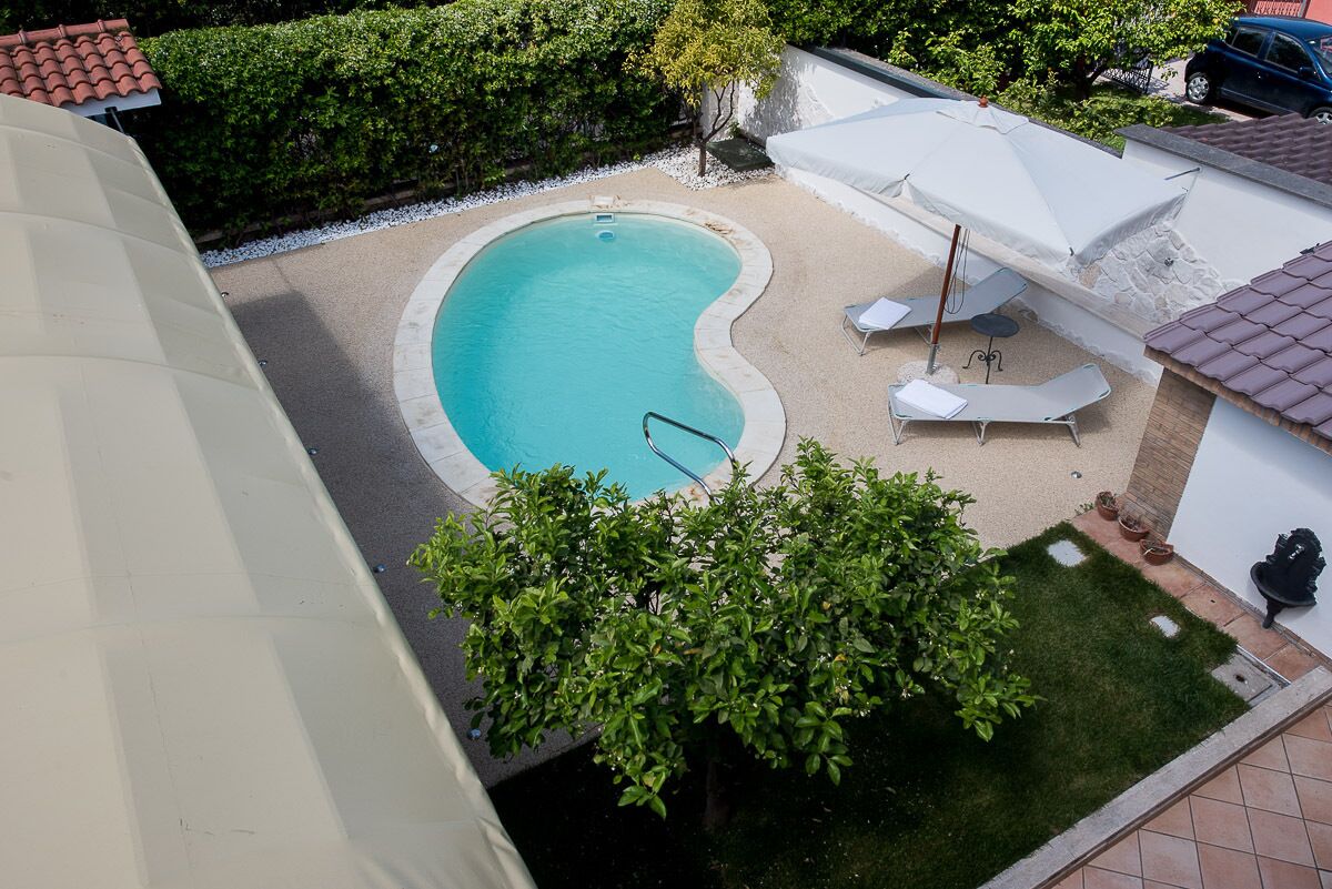 Una piscina de vora corbada, envoltada per una zona de sorra i un petit tram de gespa. Hi ha gandules i ombrelles a prop de la piscina.