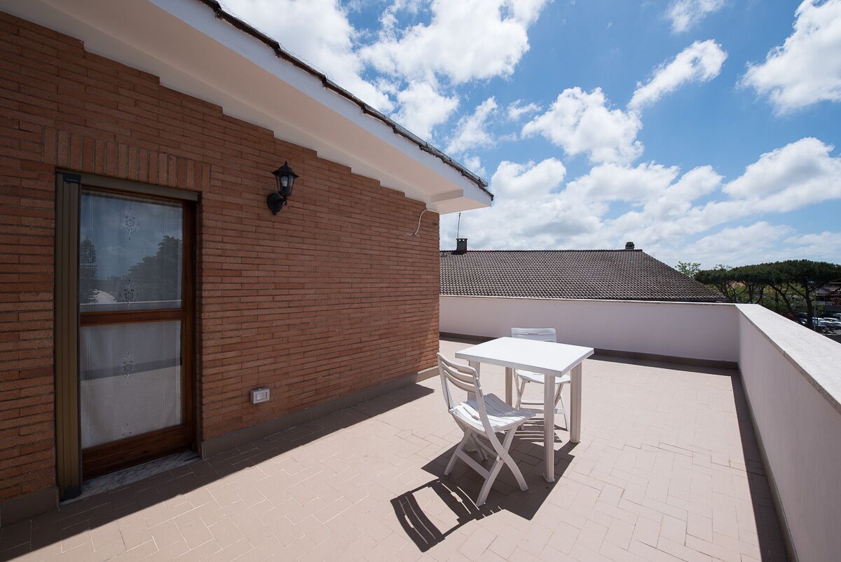 A balcony with a white table and chairs, a brick wall, and a clear blue sky with clouds.
