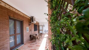 A covered patio with a brick wall, a sliding glass door, wicker furniture, and an air conditioning unit. - VILLA IARA IN CERVETERI WITH PRIVATE SWIMMING POOL (Cerveteri)