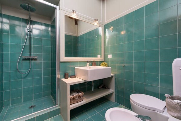 Et badeværelse med turkise fliser, en hvid vask, et spejl, en bruseniche og et toilet.