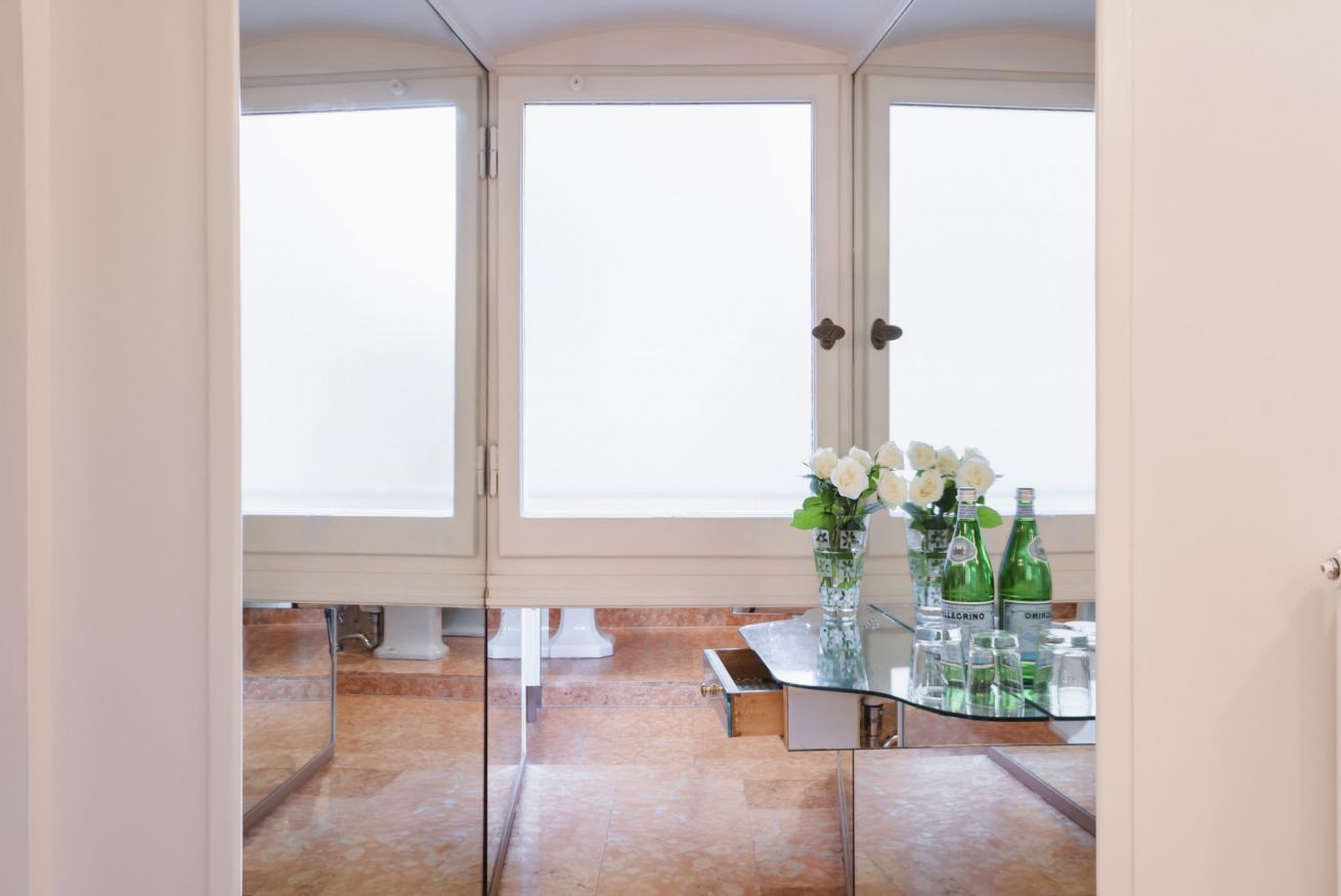 A room with a glass table, white flowers, and green bottles.