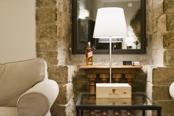 A room with a stone wall, a white lamp, a bottle, and a box on a glass table.