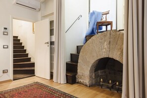 Una escalera que lleva a un segundo piso, una chimenea de piedra con repisa, y un suelo de madera.