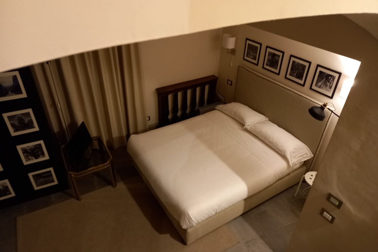 A hotel room with a bed, a chair, a lamp, and a wall with framed pictures.