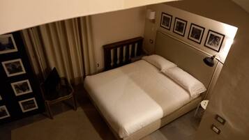 A hotel room with a bed, a chair, a lamp, and a wall with framed pictures.