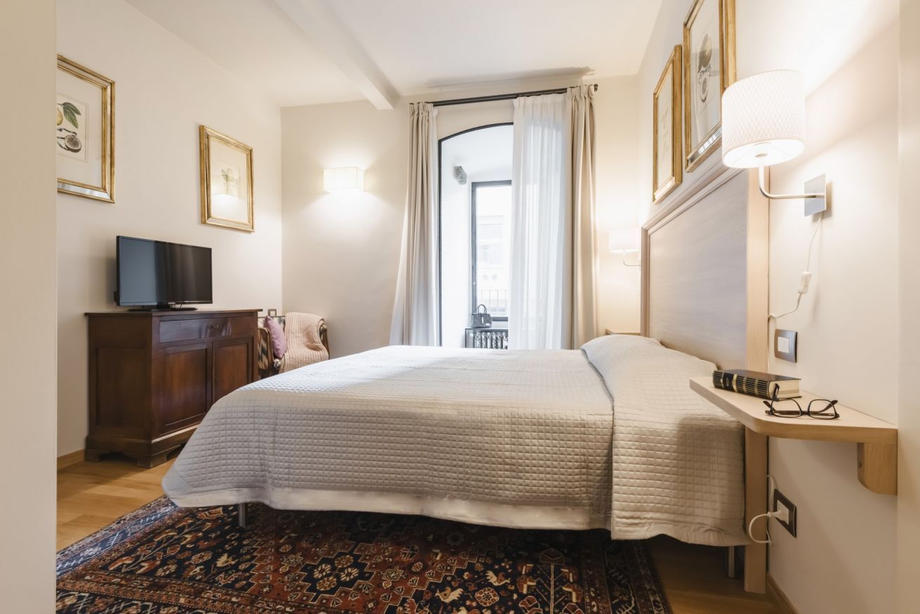 Un dormitorio con cama, televisor, escritorio y ventana con cortinas.