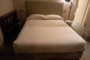 Una cama individual con cabecera, una mesita de noche con lámpara y un mueble auxiliar.