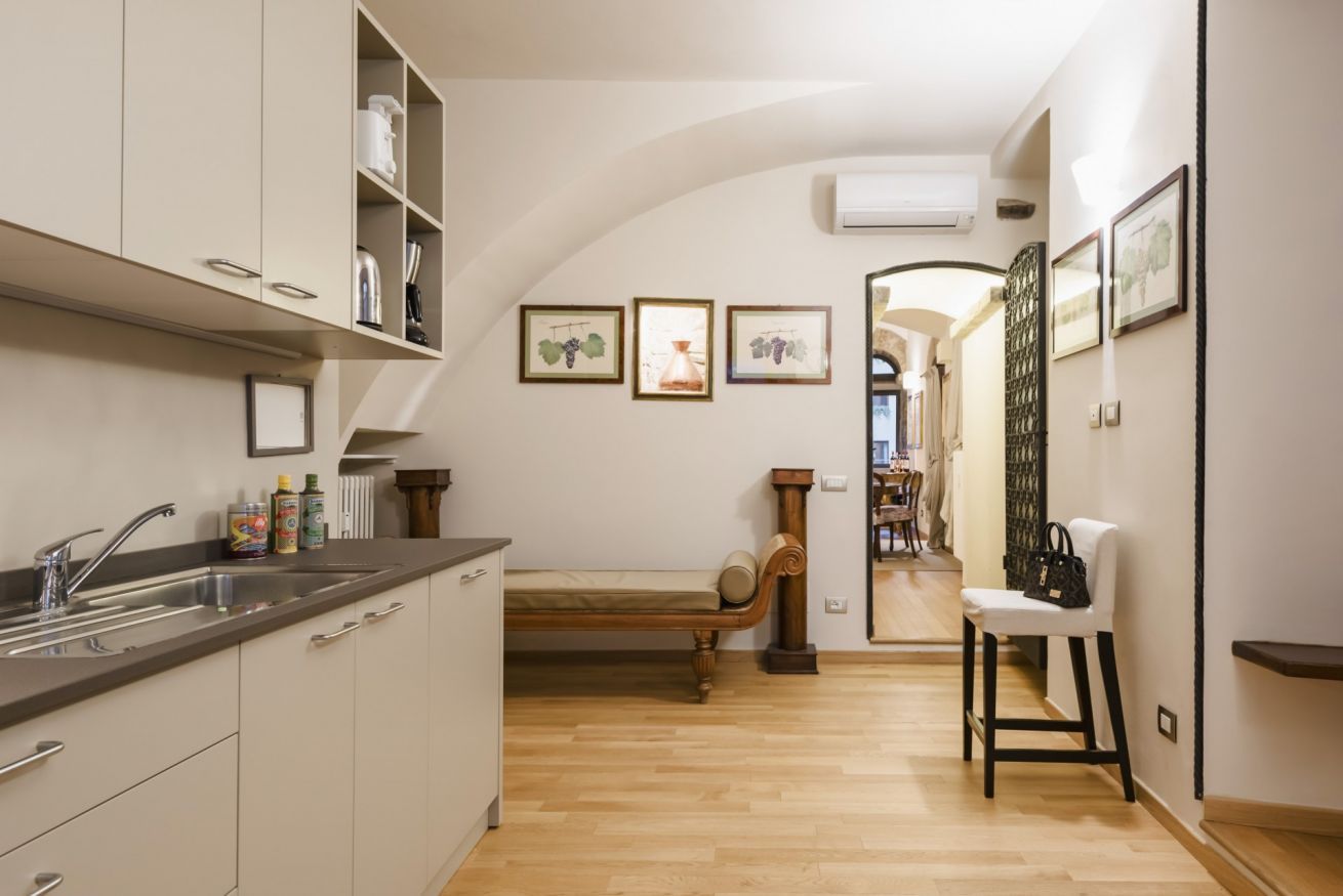 A kitchen with a wooden bench, a sink, and a chair. There are framed pictures on the wall and a radiator.