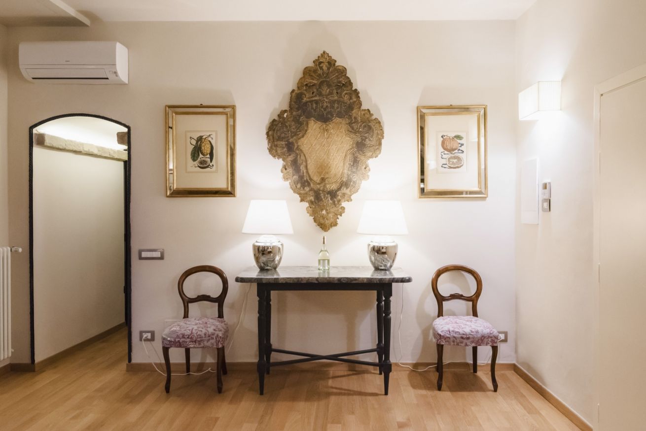 A room with a wooden floor, a table with two chairs, a wall-mounted air conditioner, and two framed pictures.