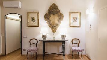 A room with a wooden floor, a table with two chairs, a wall-mounted air conditioner, and two framed pictures.