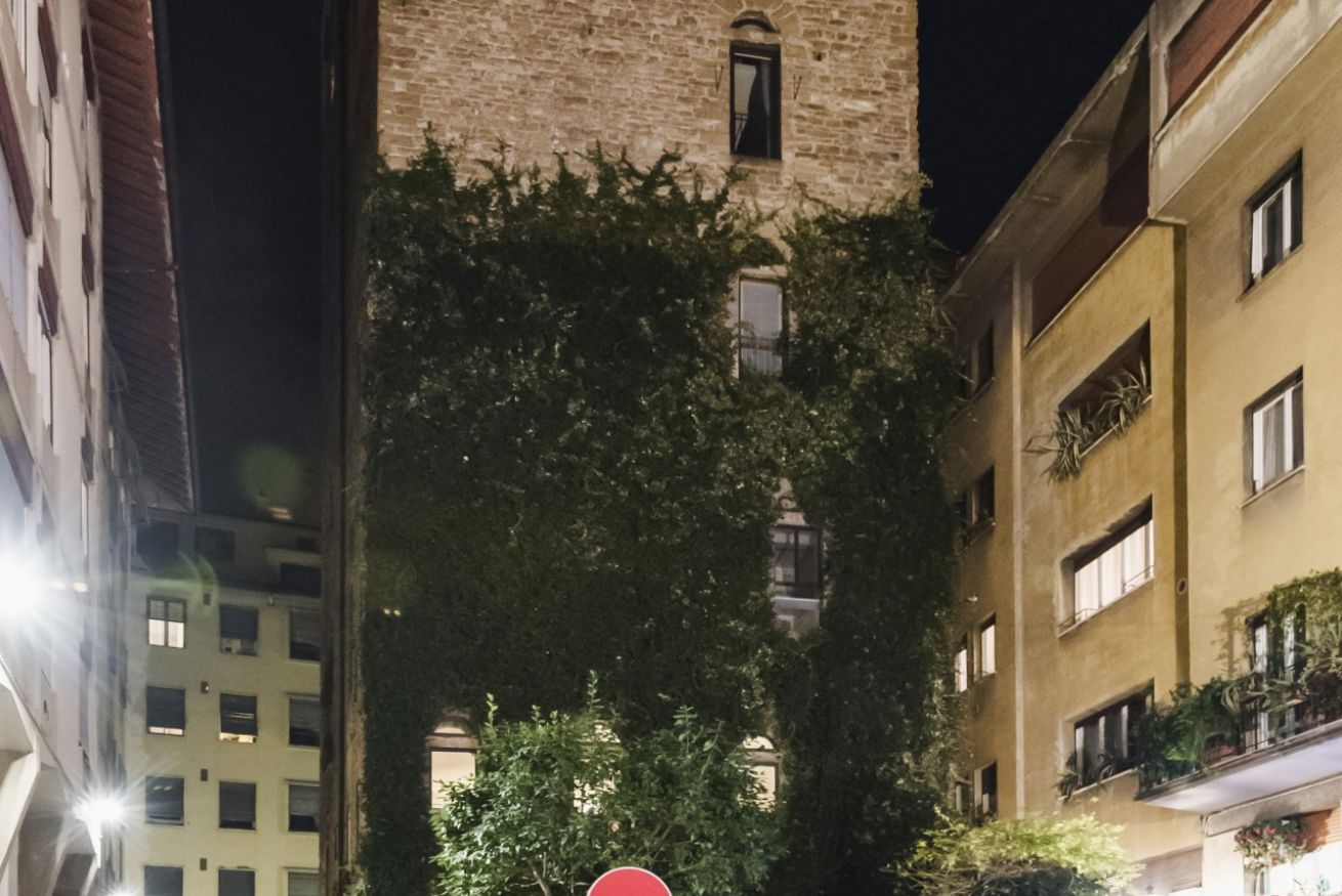 A narrow street with a tall building featuring a tower and a red stop sign.