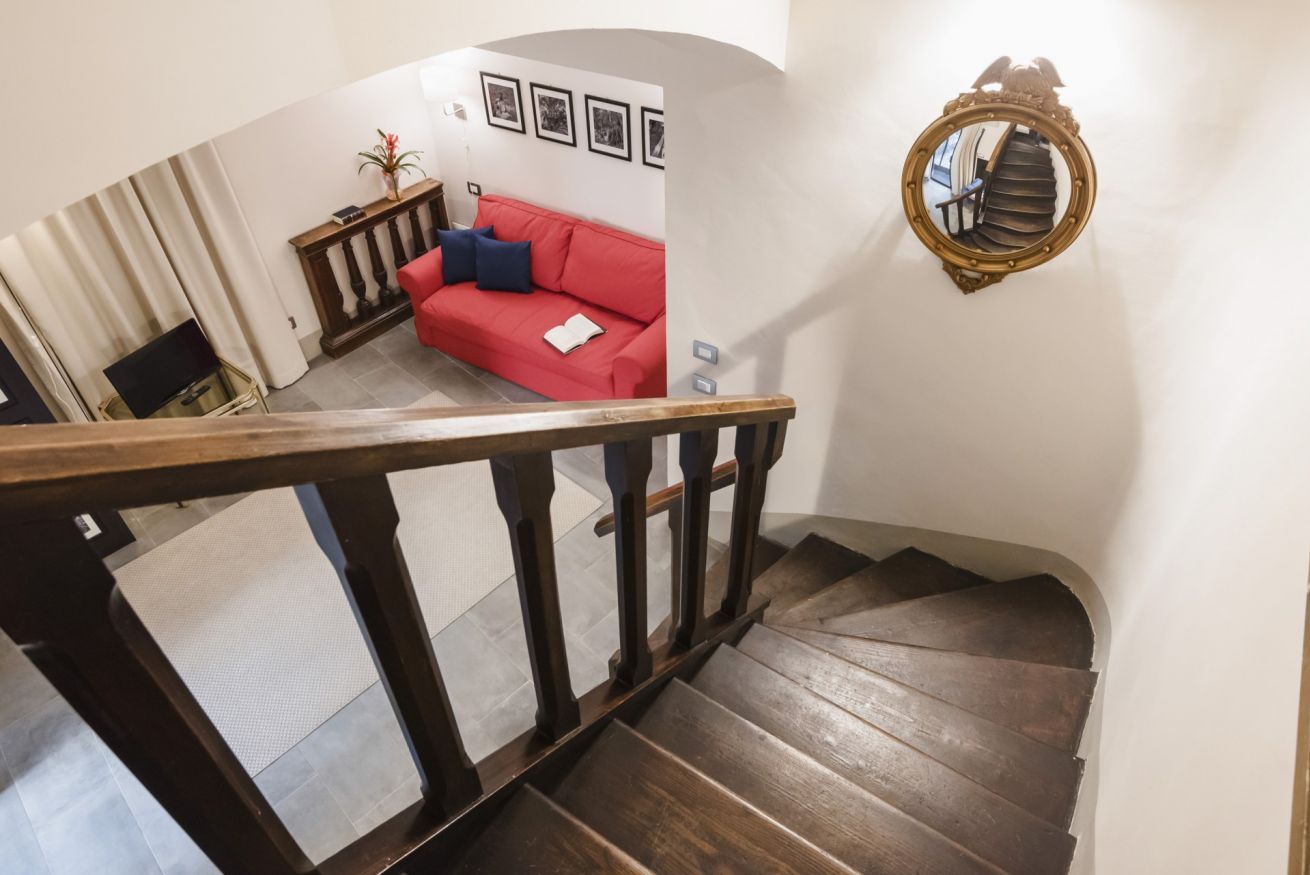 A wooden staircase with a red couch and a wall-mounted mirror in a living area.