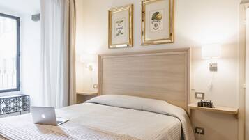 Una camera d'albergo con un letto, un portatile sul letto, due quadri appesi alla parete, un comodino con una lampada e una finestra con tende.