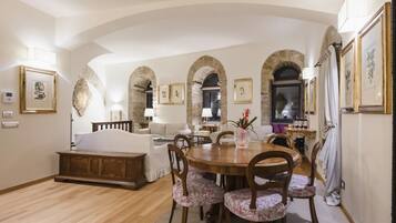 Un salón amplio con una mesa de comedor de madera, sillas con estampado floral y un sofá. Se observan puertas de arco y cuadros en las paredes.