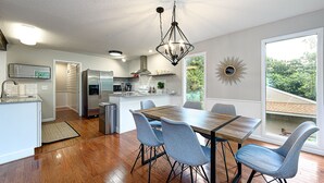 A modern kitchen with a dining area, stainless steel appliances, and a large window offering a view of greenery. - Treetop house with direct access to bike trails and small walk to Lake Avalon (Bella Vista)