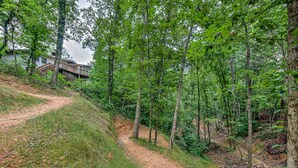 A forested area with a dirt path leading to a house with a wooden deck. - Treetop house with direct access to bike trails and small walk to Lake Avalon (Bella Vista)