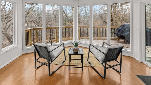 A sunroom with large windows, a ceiling fan, and two chairs with a small table and plant in the center. - Treetop house with direct access to bike trails and small walk to Lake Avalon (Bella Vista)