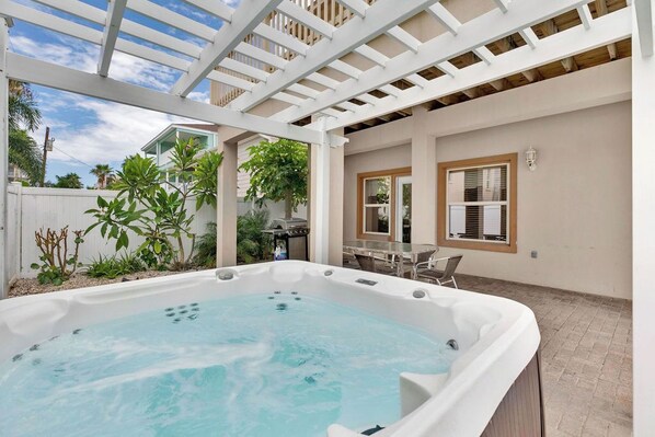 Ein Whirlpool in einem überdachten Außenbereich mit einer Pergola, einem Esstisch und Stühlen.