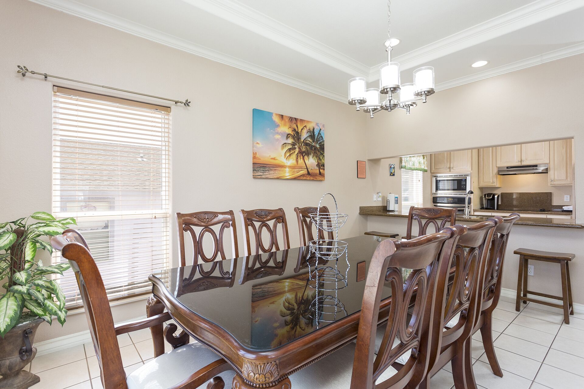 A dining area with a glass-top table and wooden chairs, a kitchen with modern appliances, and a large window with blinds.