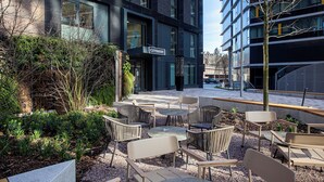 Un espace extérieur aménagé avec des tables et des chaises, entouré de verdure et bordé d’un bâtiment sur lequel on peut lire l’inscription « City Suites ».