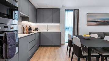 A modern kitchen with grey cabinets, a built-in oven, and a dining area with a table and chairs.