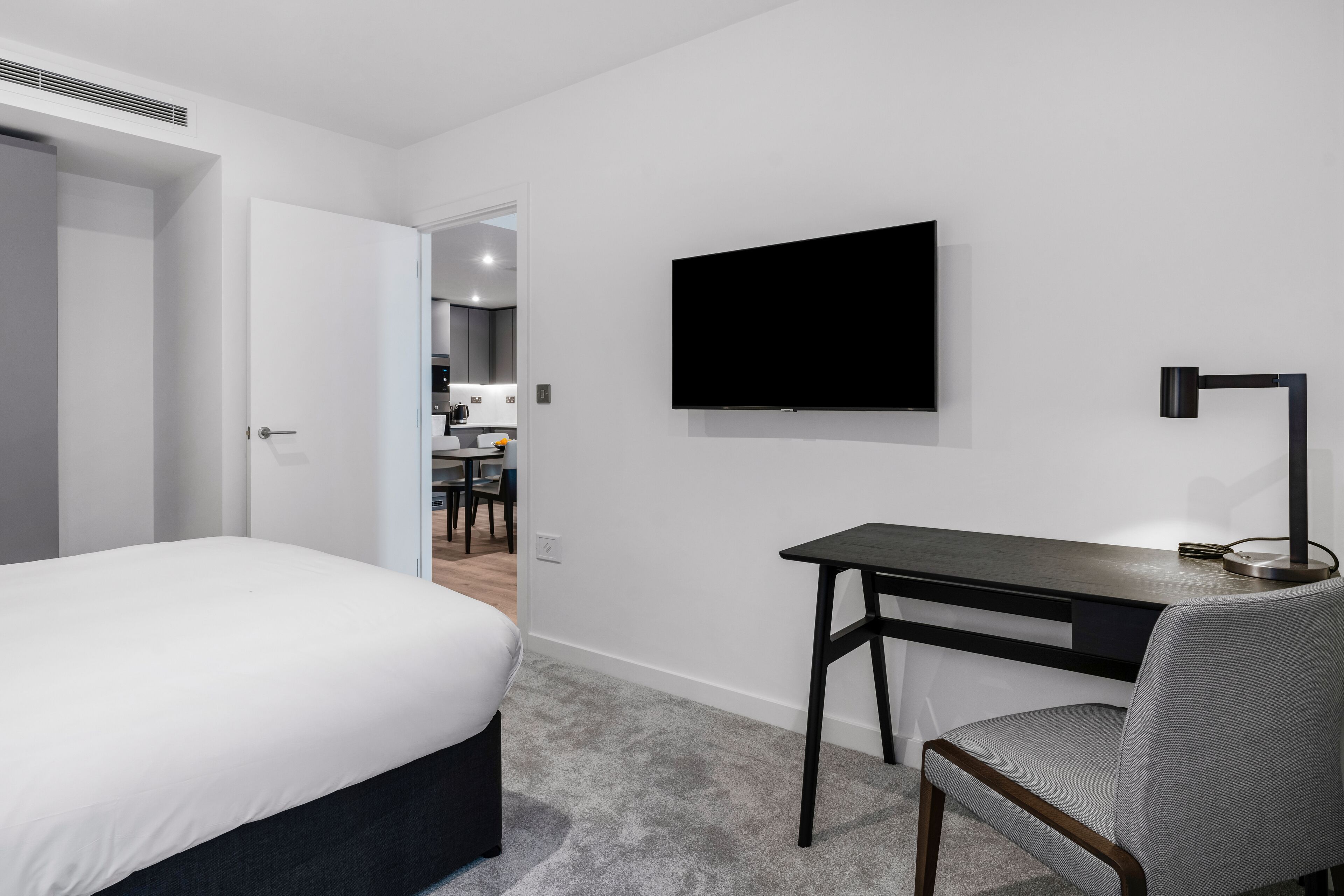 Et moderne hotelværelse med seng, skrivebord, stol, fladskærms-tv og lampe.
