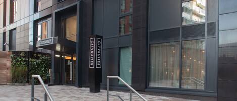 Un edificio moderno con un letrero que dice "CitySuites". Cuenta con ventanas amplias, una escalera con barandillas metálicas y un frente de ladrillo.