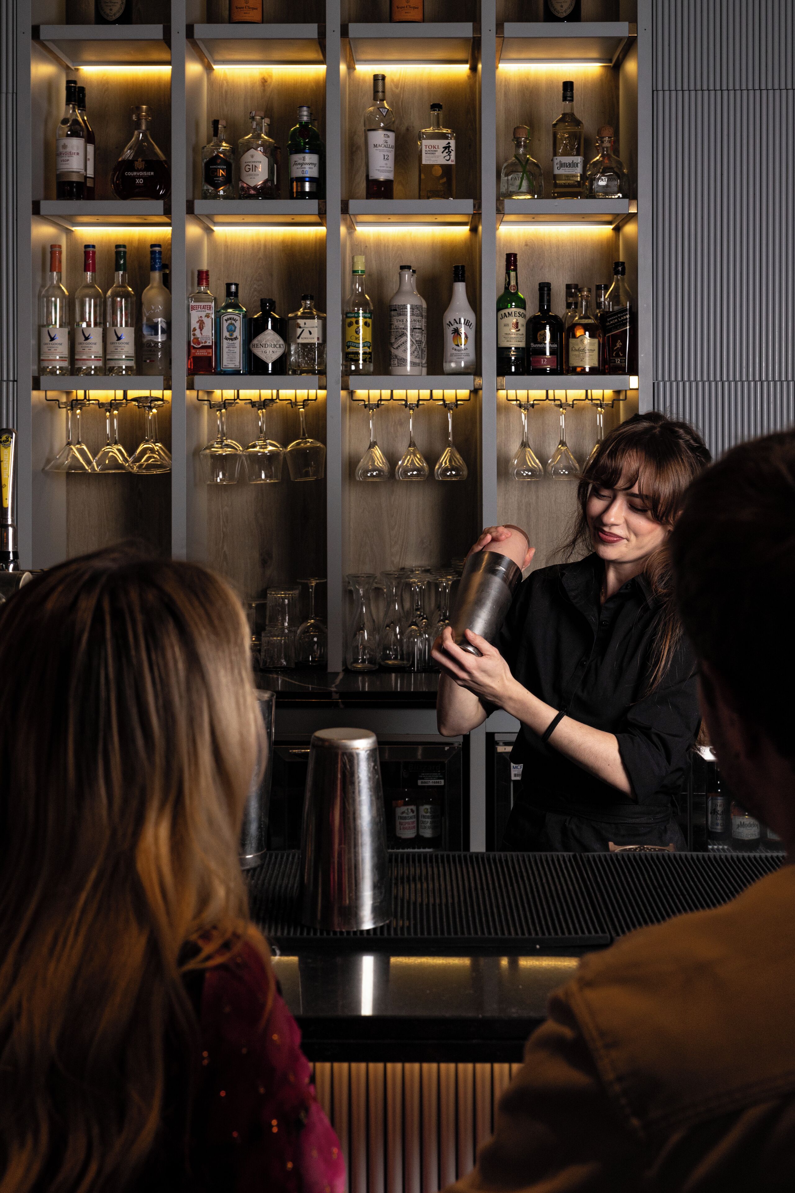 Zona de bar con estantes llenos de botellas de licores y copas.