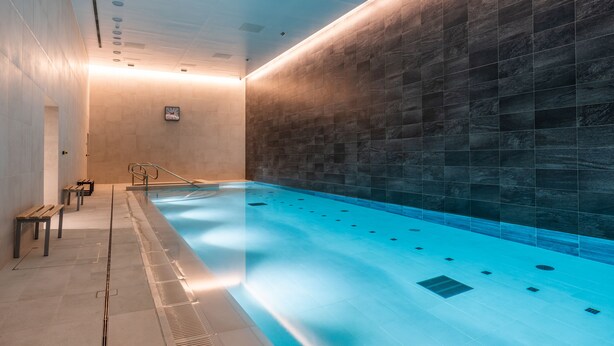Une piscine intérieure avec un mur carrelé, des bancs et une horloge.