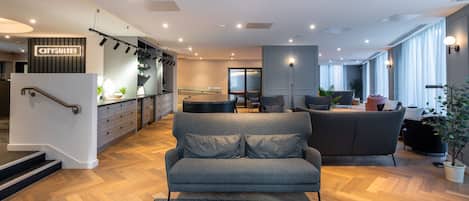Un intérieur d’hôtel moderne avec un canapé, un coin repas et un escalier.