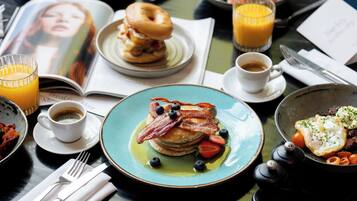 A breakfast table with pancakes, bacon, blueberries, and a plate of eggs.