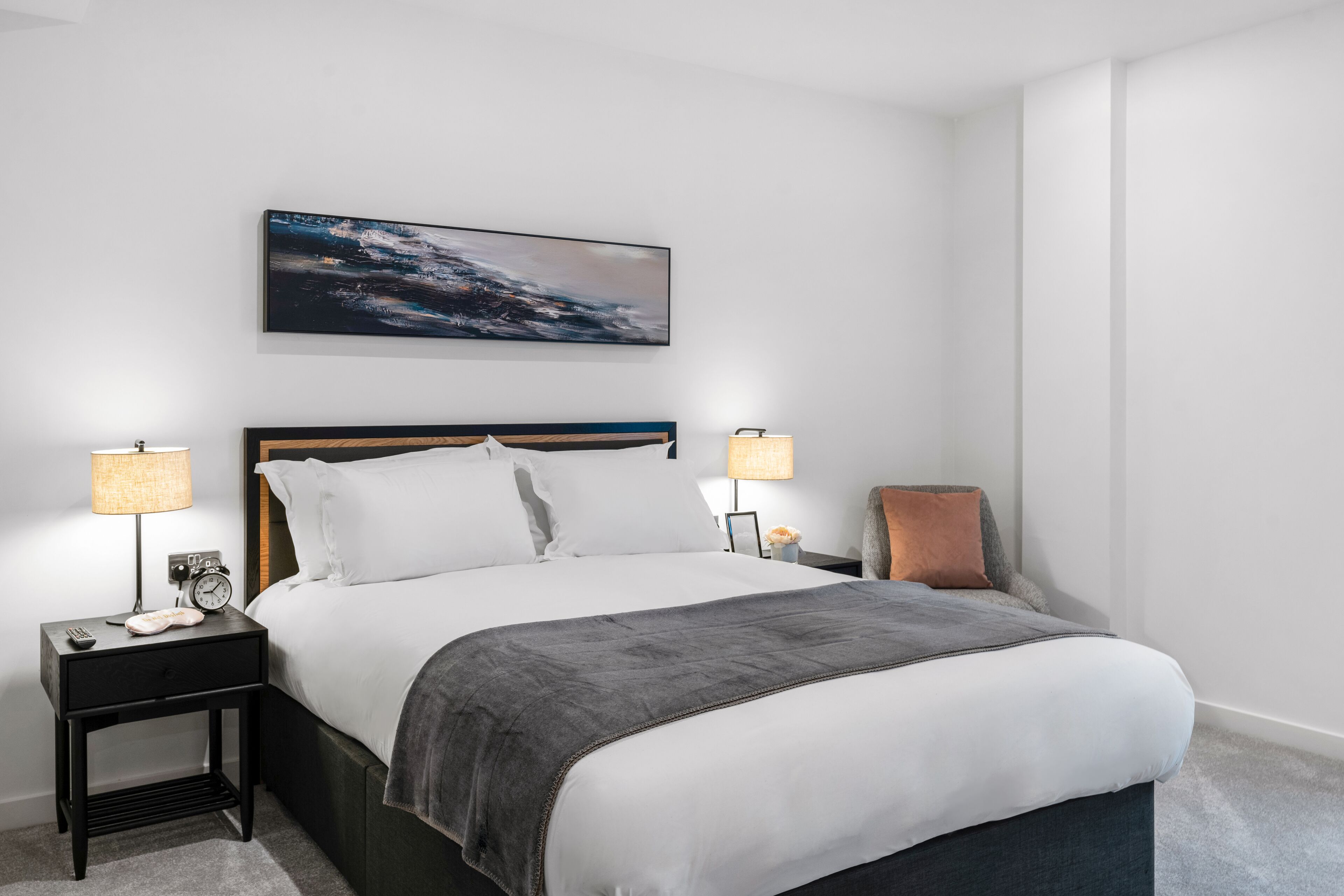 A neatly arranged hotel room with a large bed, two bedside tables with lamps, a chair, and a painting on the wall.