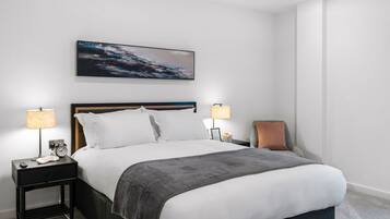 A neatly arranged hotel room with a large bed, two bedside tables with lamps, a chair, and a painting on the wall.