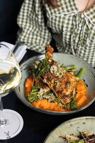 Un plato de pollo asado con verduras y una copa de vino blanco.