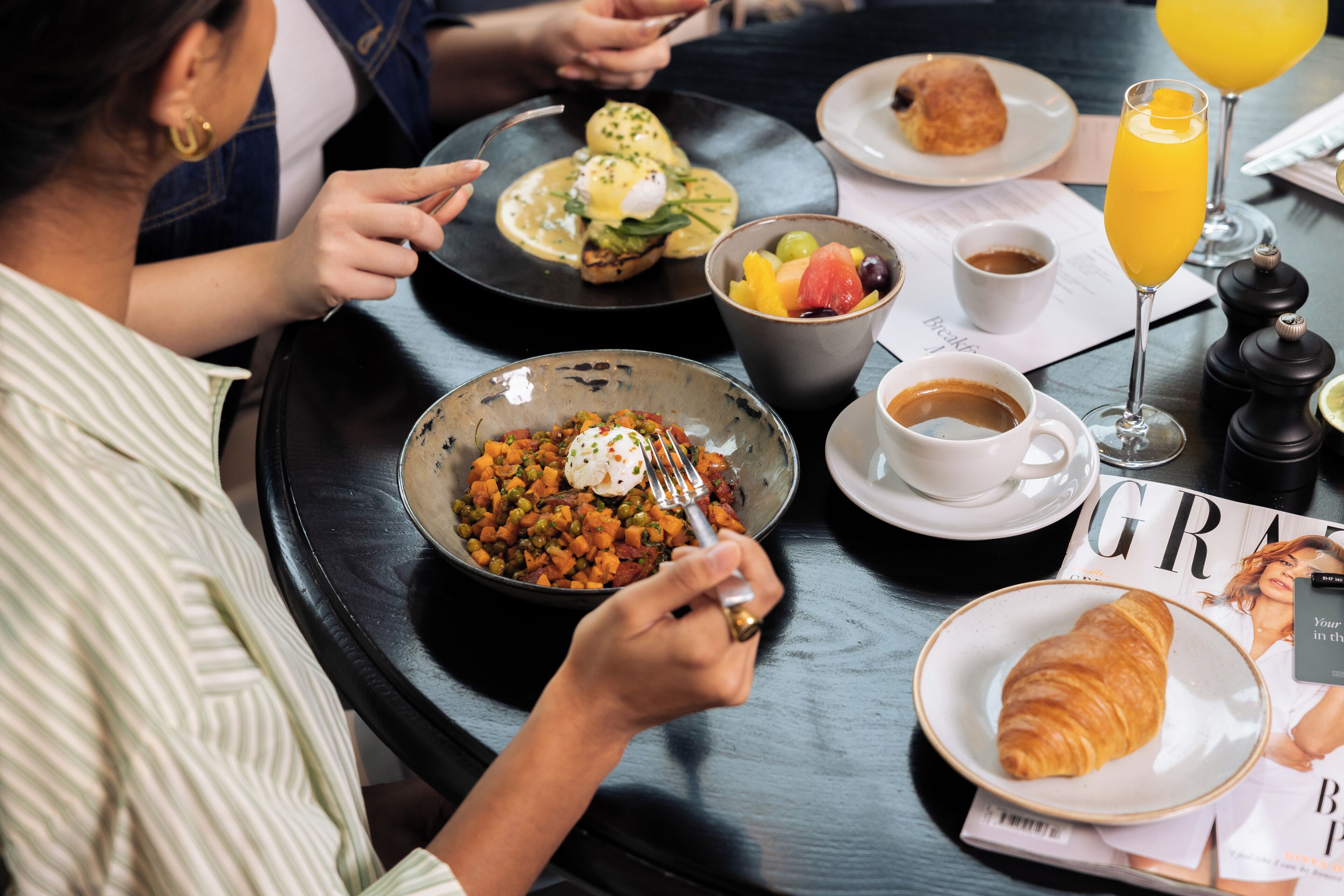 Une table à manger avec divers aliments pour le petit-déjeuner, notamment un croissant, un bol de soupe, un saladier de fruits et un verre de jus d’orange.