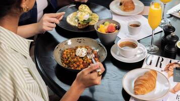 Une table à manger avec divers aliments pour le petit-déjeuner, notamment un croissant, un bol de soupe, un saladier de fruits et un verre de jus d’orange.