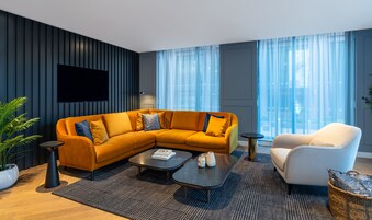 Una sala de estar moderna con un sofá modular, una mesa de centro, un sillón blanco y un televisor montado en la pared.