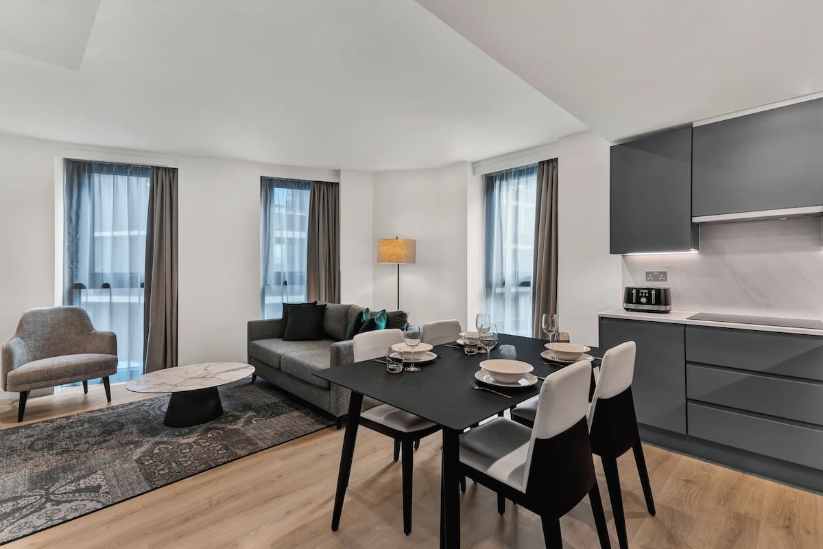 A modern living room with a dining table set for four, a sofa, a coffee table, and a kitchen area with a microwave.