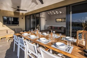 A dining area with a long wooden table set for a meal, a sofa, and a view of the cityscape.