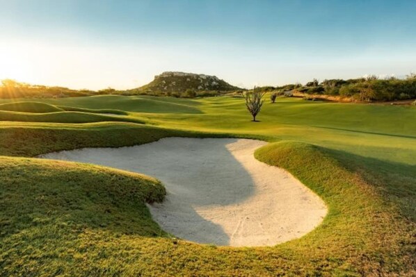 Un parcours de golf avec des bunkers de sable, un ciel dégagé et une colline qui se dessine à l’horizon.