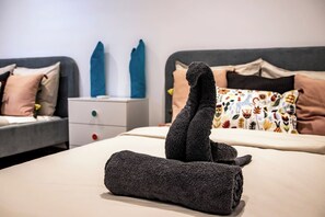Un lit bien fait, avec une serviette enroulée posée au centre, une table de chevet avec un tiroir et un oreiller à motifs sur le lit.