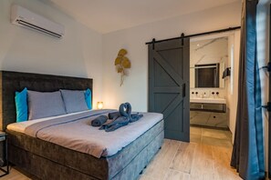 A bedroom with a bed, pillows, a wall-mounted air conditioner, a bedside lamp, and a towel arrangement.