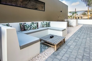 A modern outdoor seating area with a wooden coffee table and cushions. - `Ocean Sunset Villa` luxury stay max. 14 people.` (Sint Michiel)