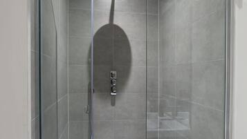 Una ducha moderna con puerta de cristal, un cabezal de ducha de mano y una toalla blanca colgada en la pared.