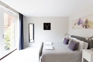 A modern bedroom with a large bed, a bedside table, a mirror, and a window with curtains. - Immaculate Central Windsor Town House (Windsor)