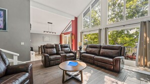 A spacious living room with leather sofas, a wooden coffee table, and large windows offering a view of the outdoors.