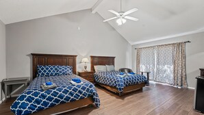 A bedroom with two beds, wooden flooring, a ceiling fan, and a window with curtains.
