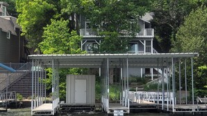 A waterfront property with a covered dock, a small boat shed, and a house with a balcony overlooking the water.