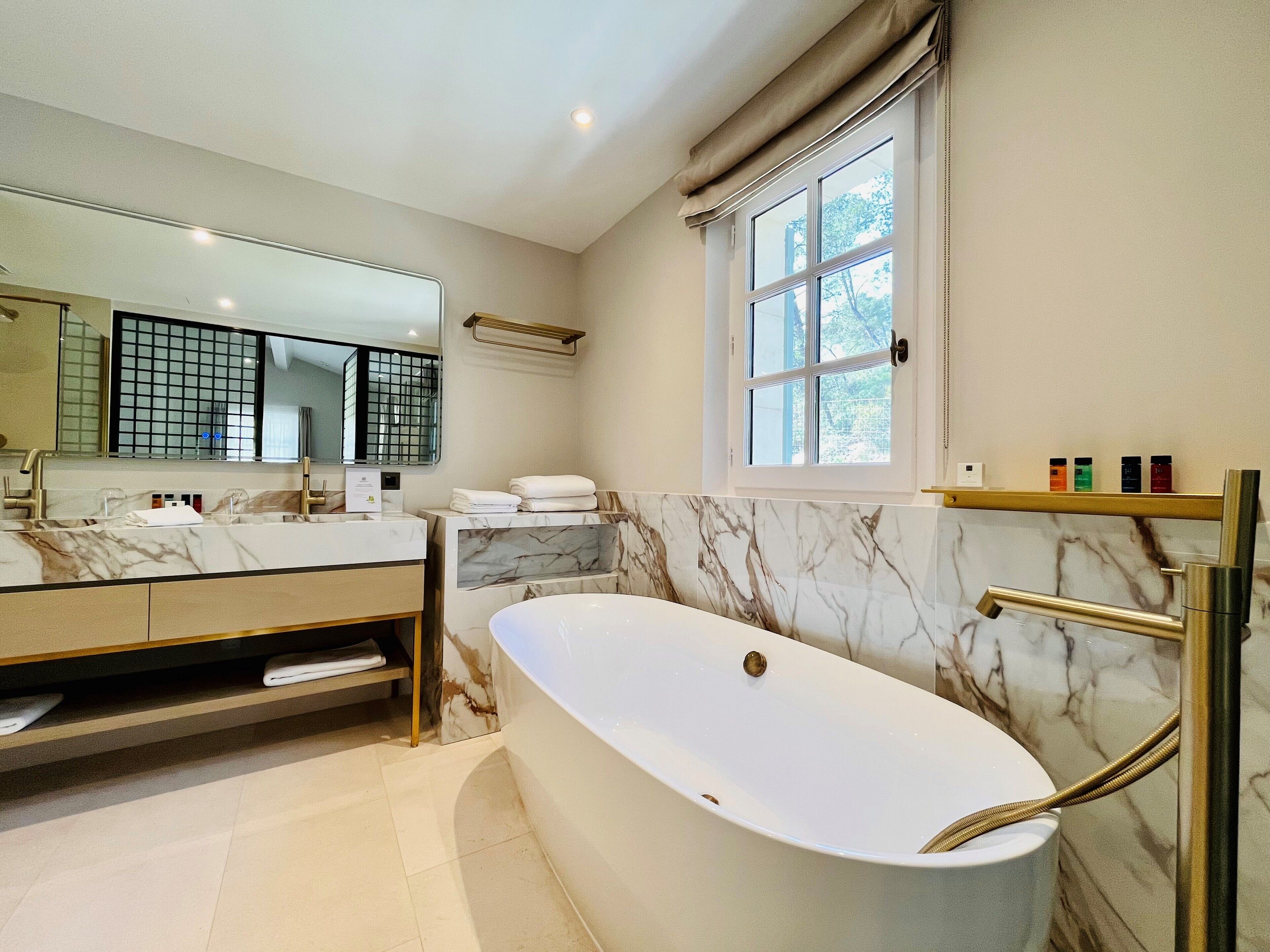 A modern bathroom with a marble vanity, a freestanding bathtub, and a large mirror.